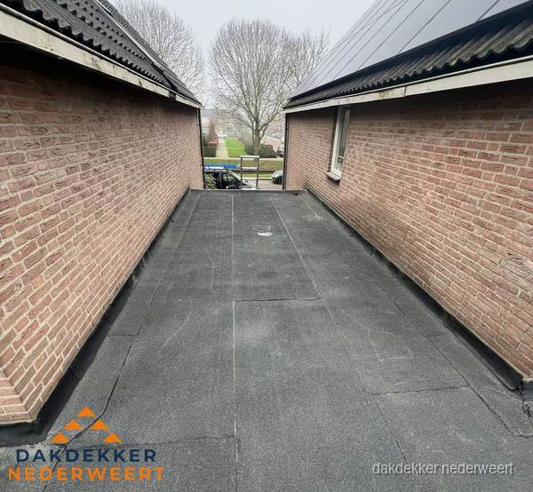 Plat dak met bitumen dakbedekking tussen bakstenen muren in Nederweert